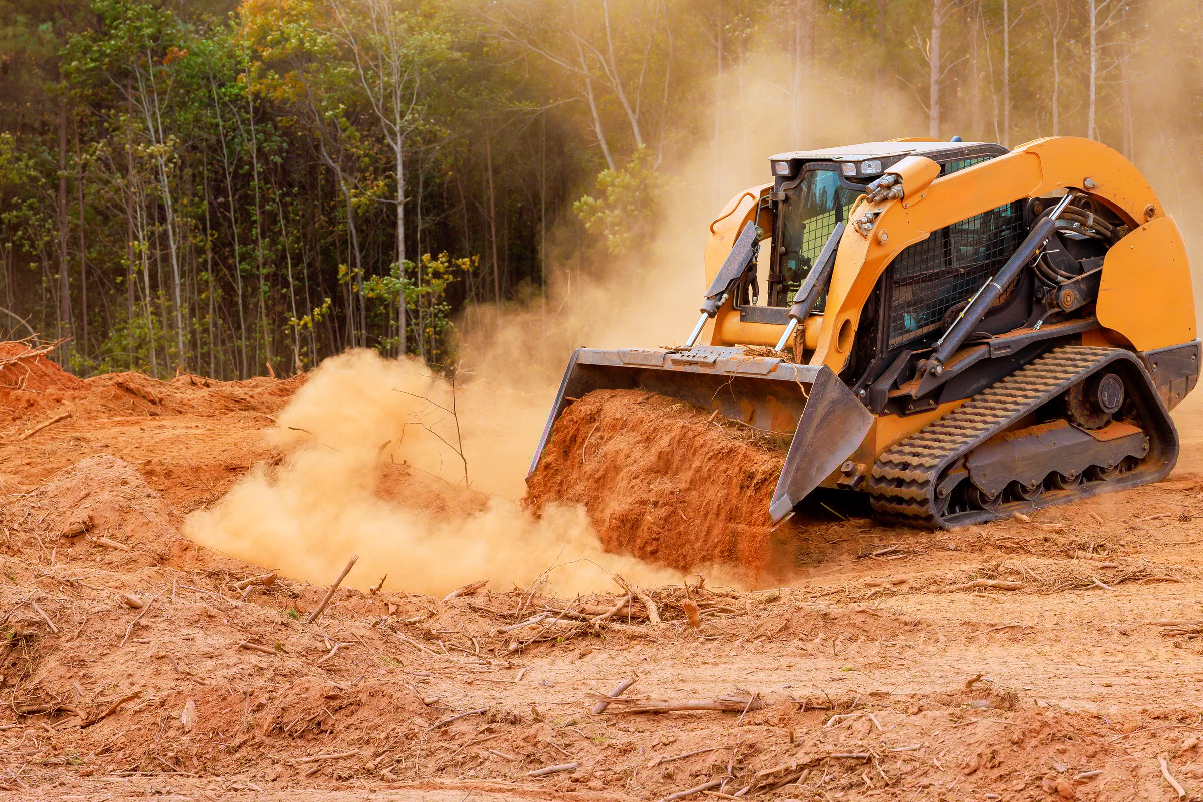 Heavy machinery clears land covered in dust among trees, preparing site for future development activities.