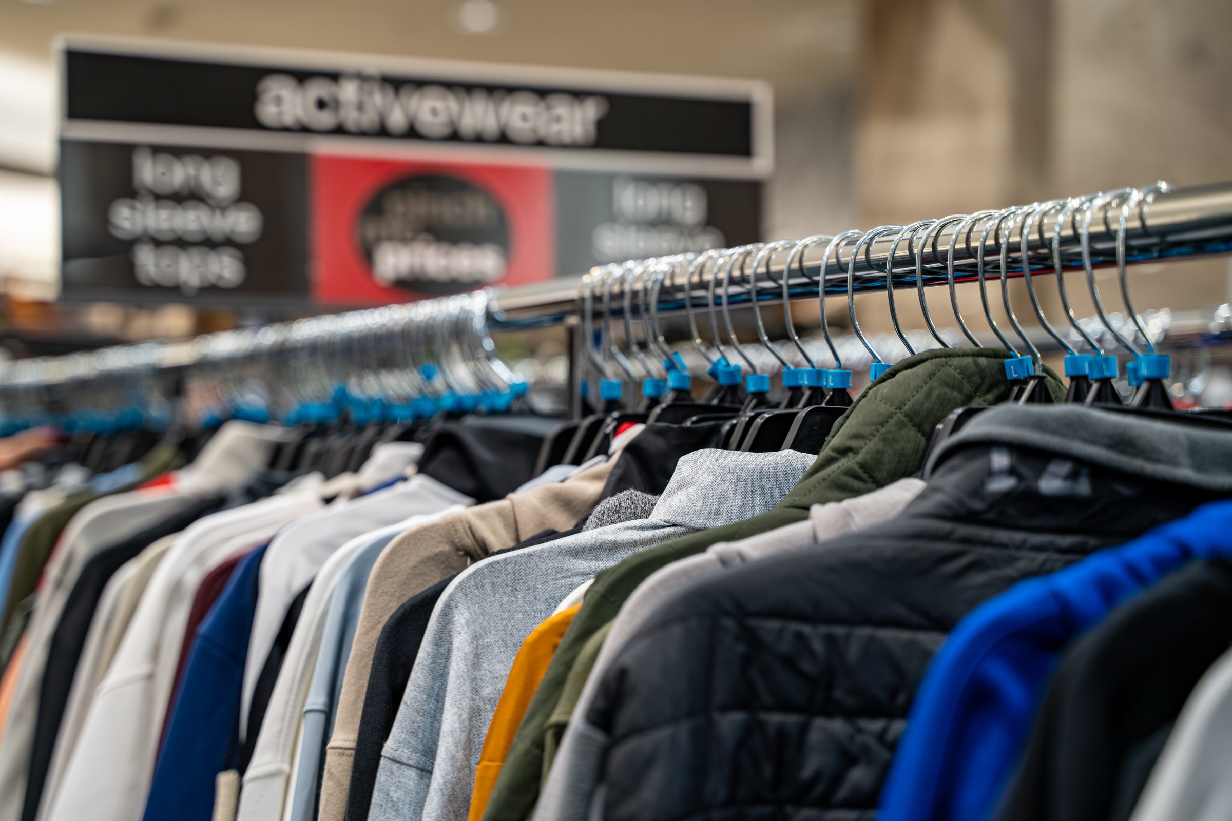 Close up of activewear jackets and tops on clothing rack inside store.