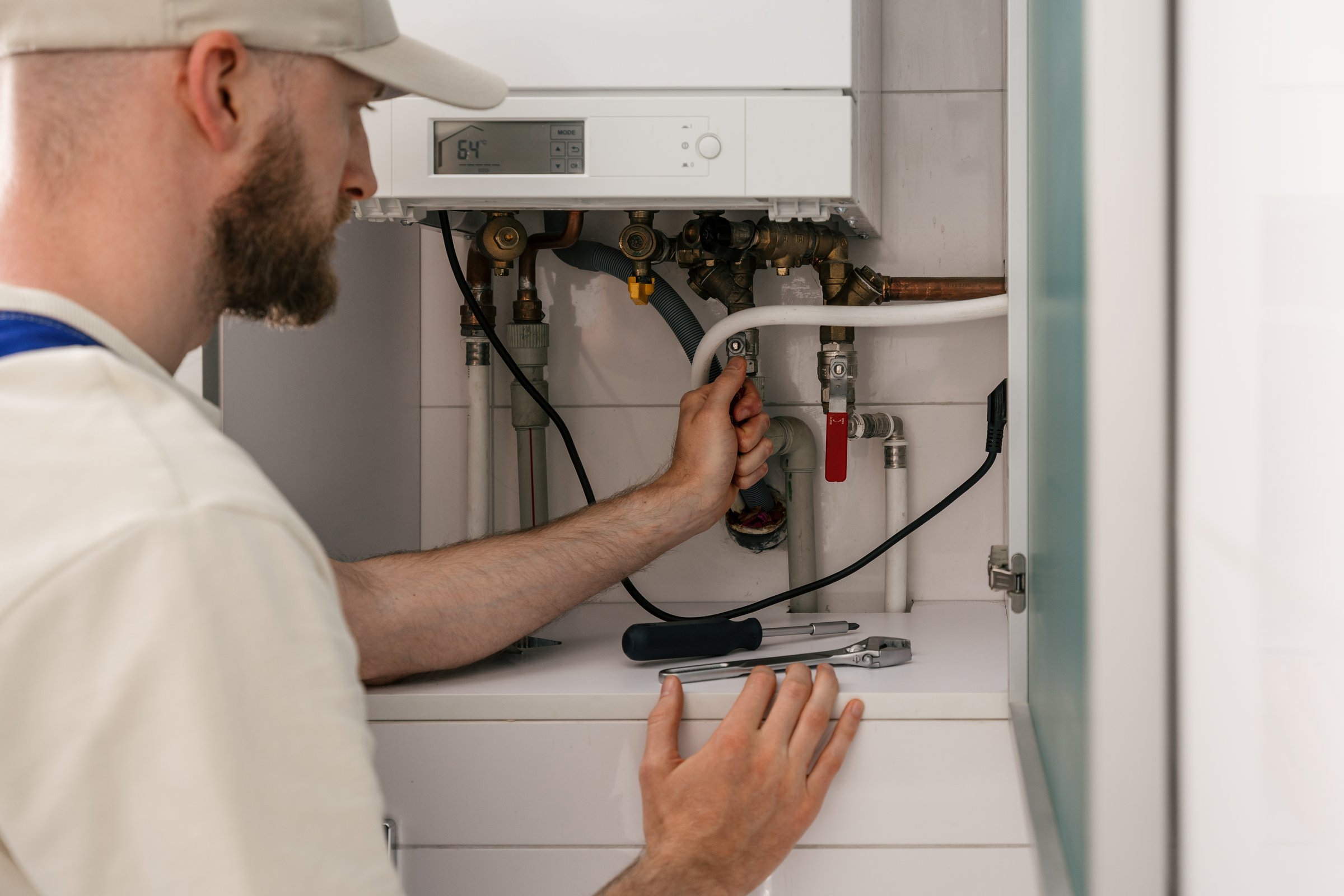 Repairman shut off valve on pipeline, conduct maintenance on gas boiler in a modern bathroom. He focused on checking connections and adjusting settings for optimal performance and energy efficiency