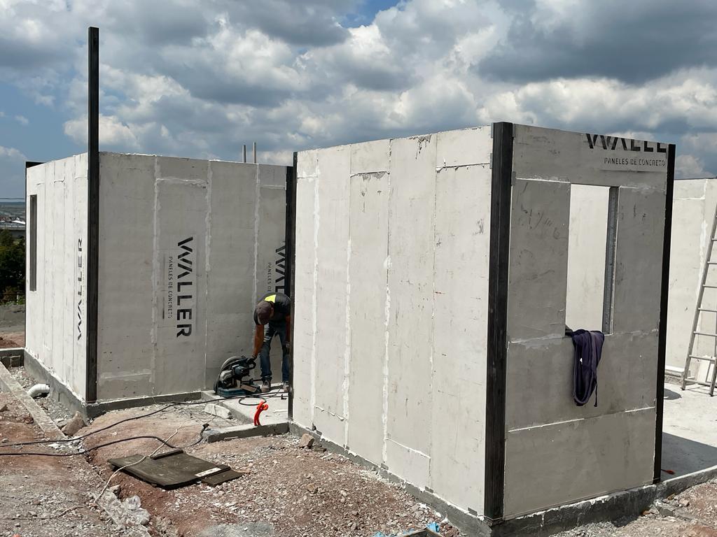 Construction worker building a concrete panel structure under cloudy skies. "Waller" logo visible on panels.