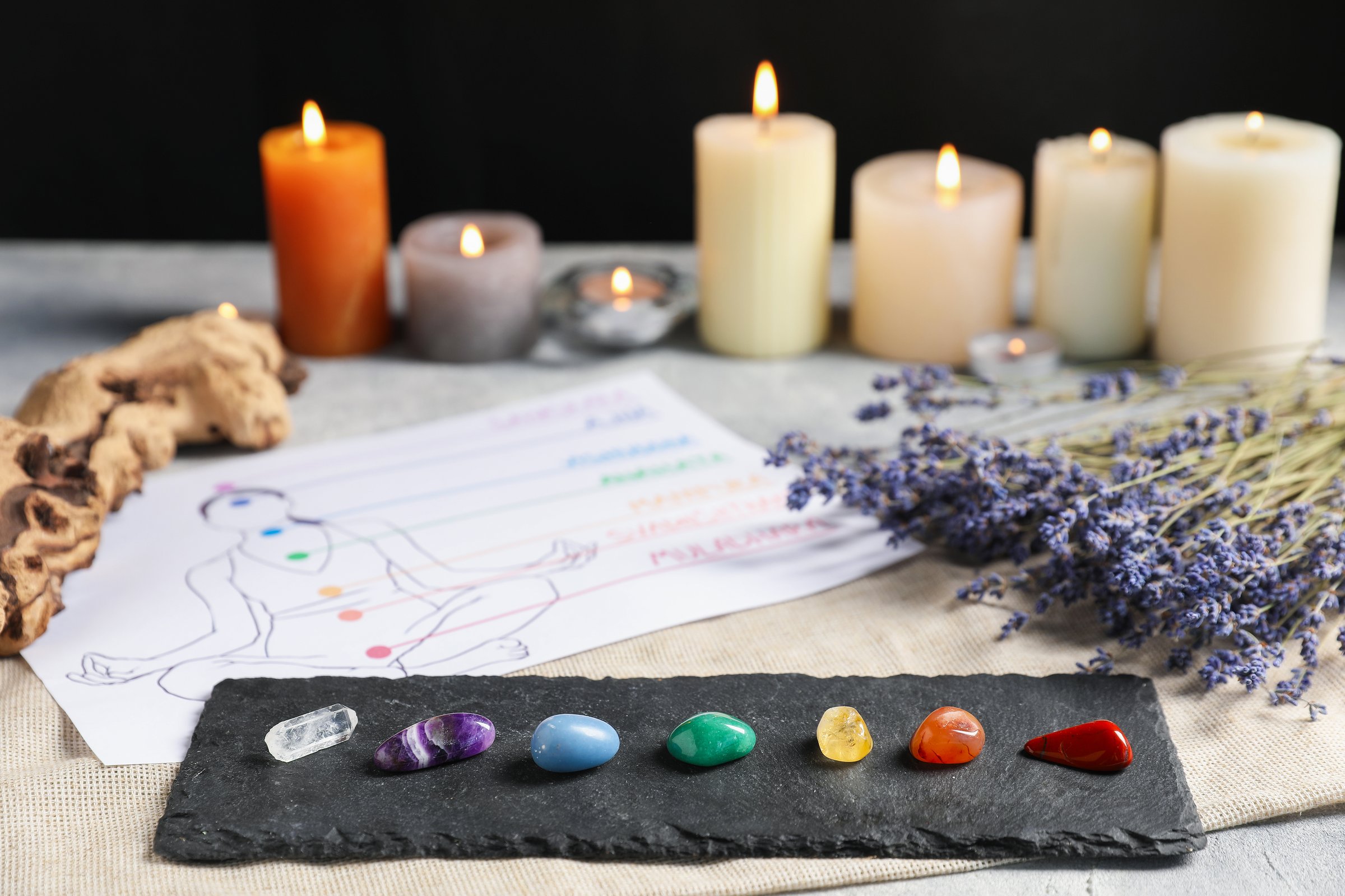 Chakra gemstones, lavender flowers, human drawing and burning candles on light table, selective focus