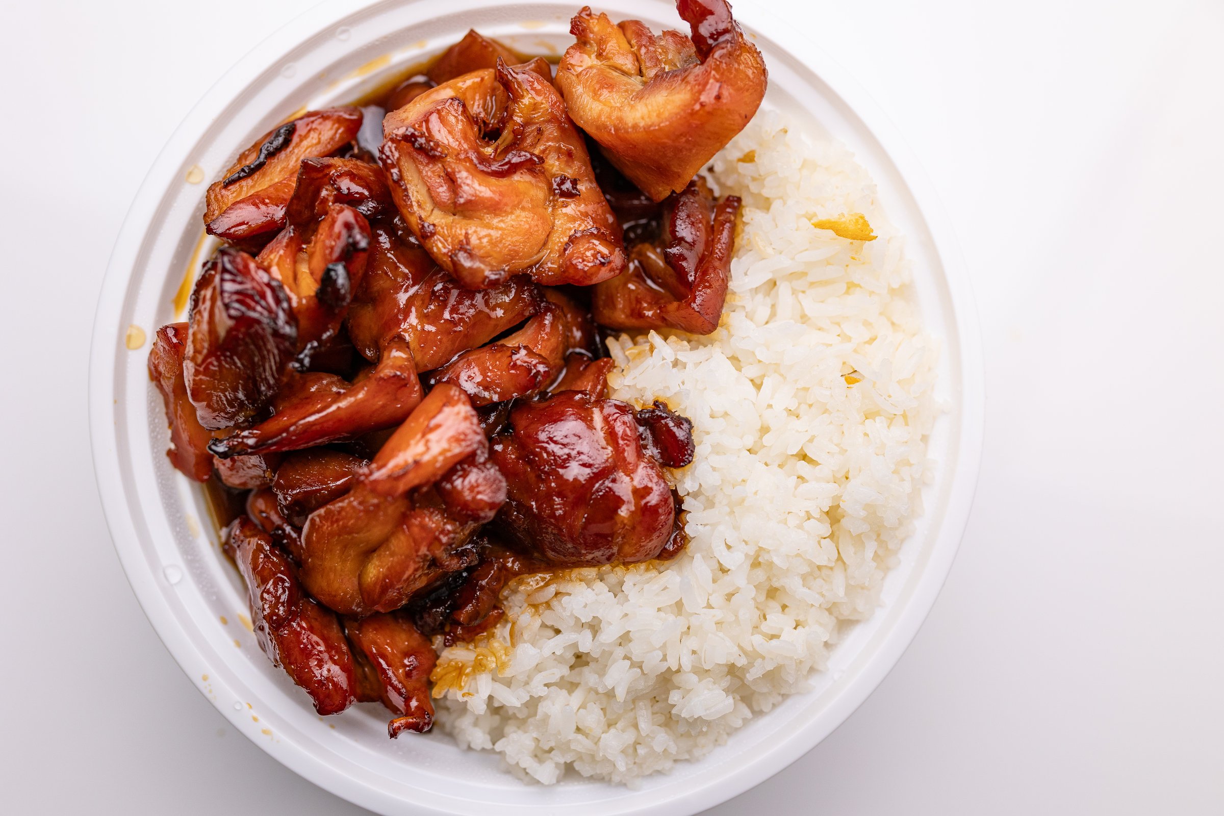 Top-down view of a plastic bowl containing Chinese takeout, featuring stir-fried chicken glazed in bourbon sauce and served with white rice.