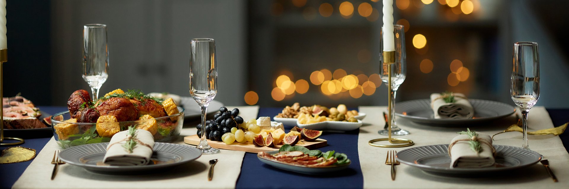 Header background shot of roasted turkey and cheese platter served with empty champagne glasses on festive dinner table with Christmas lights in blurred background