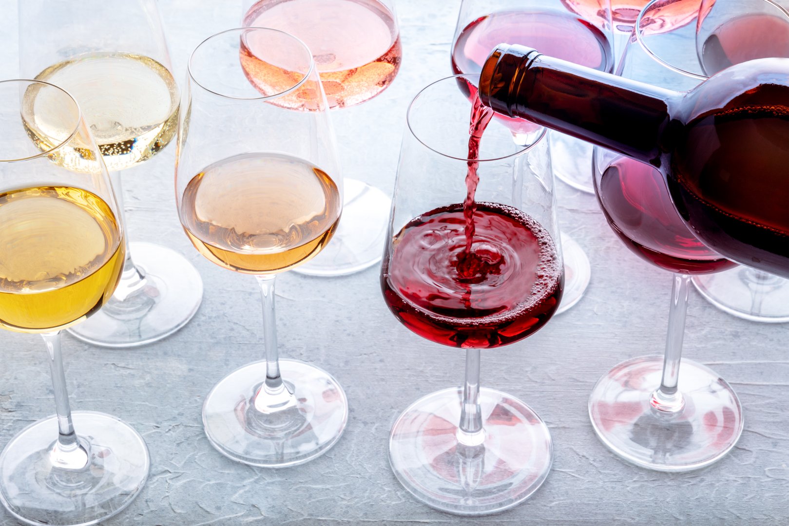 Red wine pour into a glass at a tasting. Rose, red, and white wine, drinks on a table at a winery. An assortment of wines of many different colors
