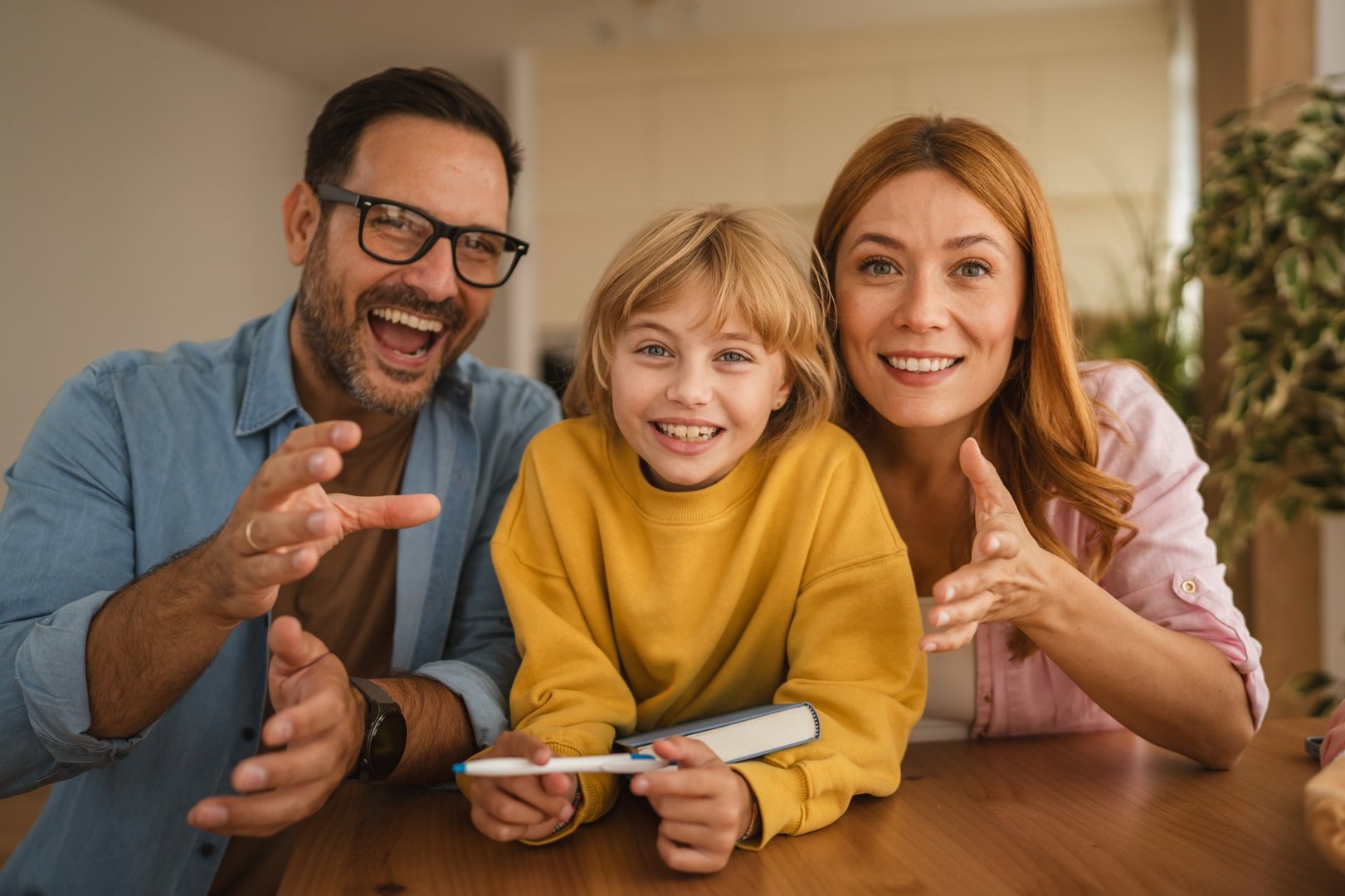 Smiling parents and their daughter enjoy quality time together while sitting at a wooden table in a cozy living room, creating joyful memories and strengthening their bond