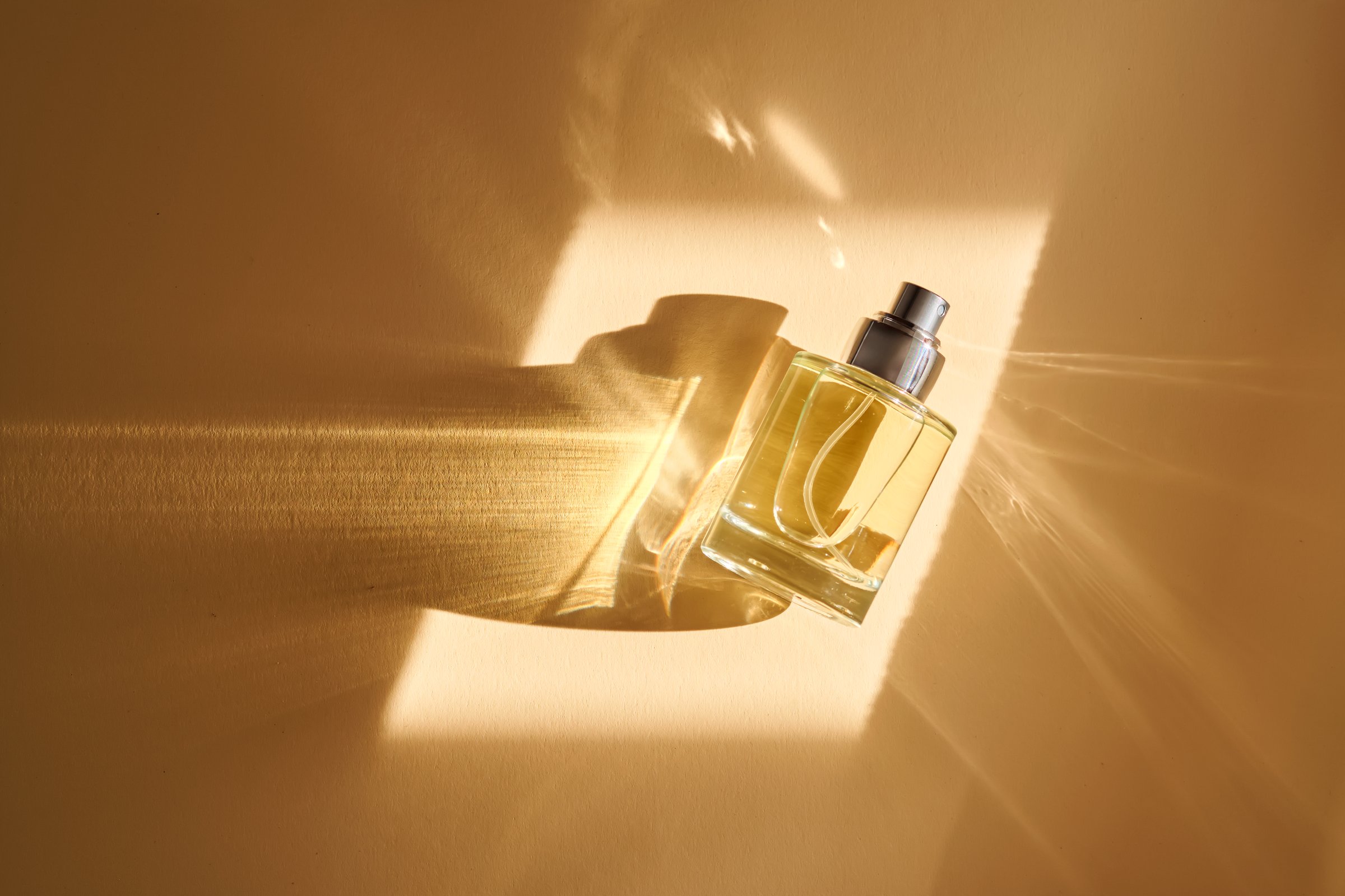 Perfume on a beige background in the rays of bright sun with beautiful highlights. High quality photo.