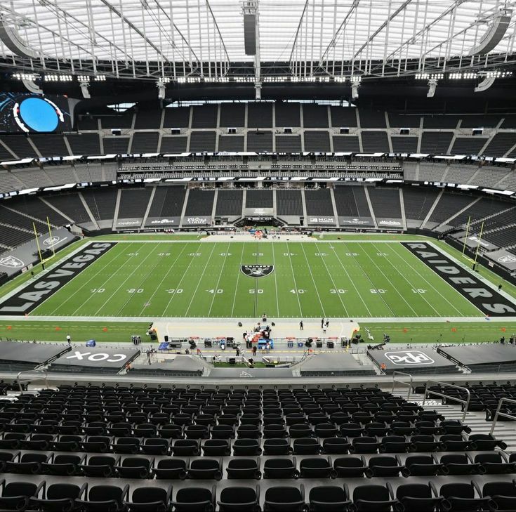 Empty football stadium with a green field, marked with Raiders and Las Vegas, surrounded by empty seats and a retractable roof.