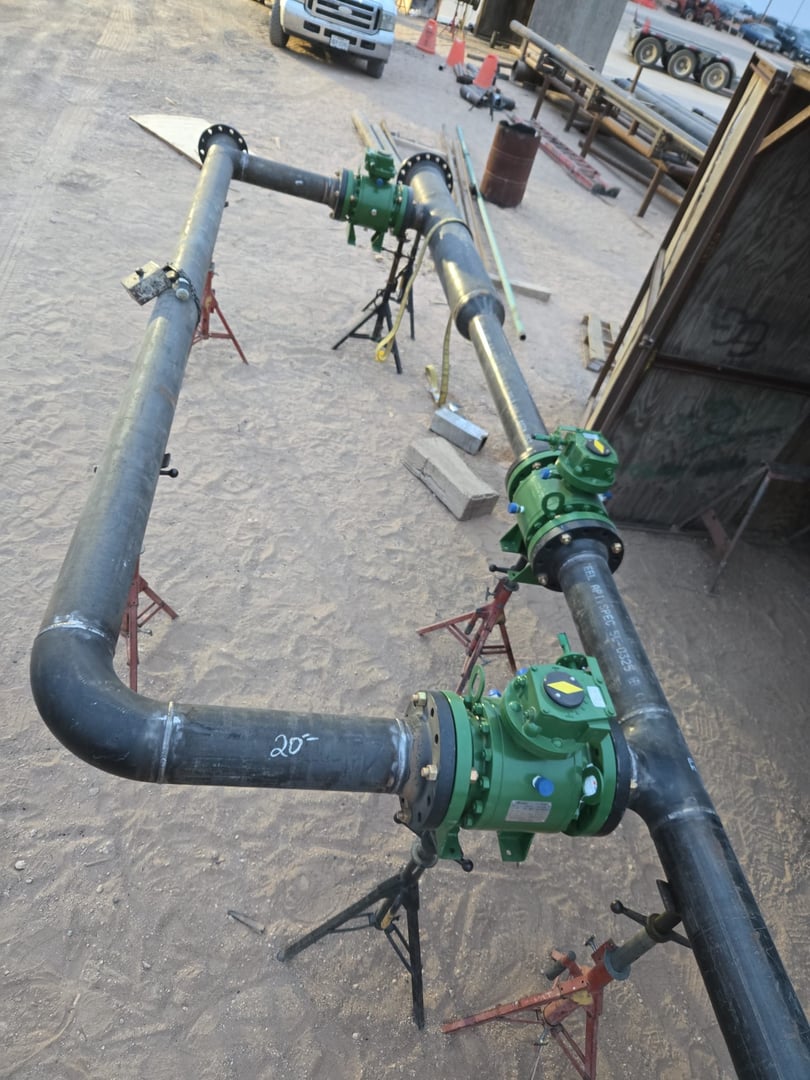 Industrial piping with green valves supported by stands on a sandy construction site.