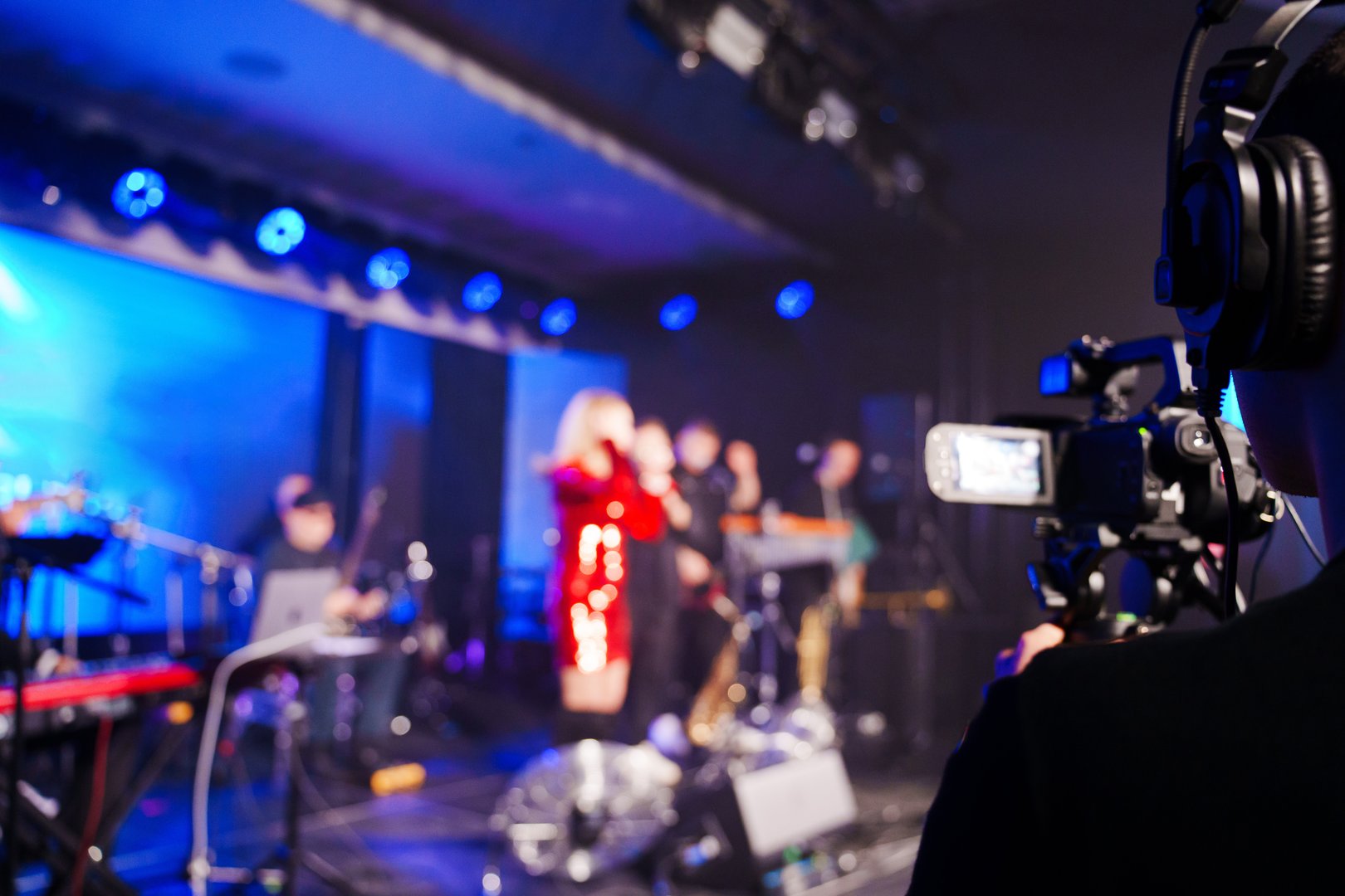 A professional videographer is filming a concert on stage. blurred artists on stage, focus on the camera. unrecognizable people.