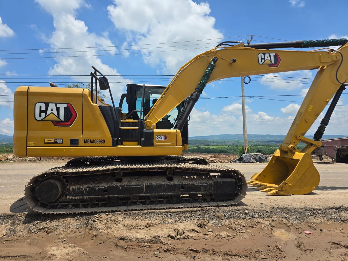 Yellow Caterpillar excavator on a construction site, sunny day, with a visible arm and bucket, and a clear sky backdrop.