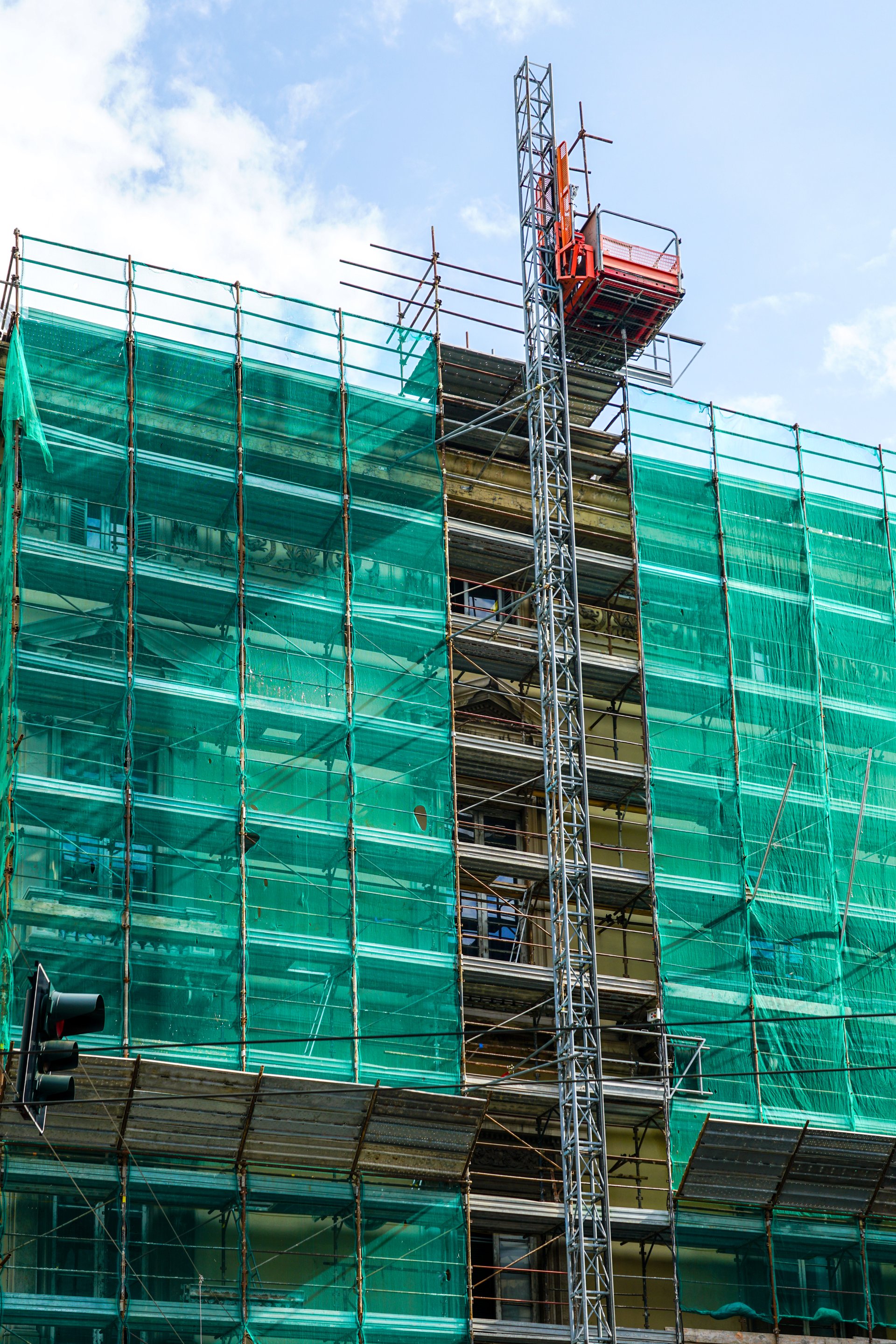 Historic house facade renovation using prefabricated metal tube scaffolding covered with green safety net, electric elevator for lifting materials