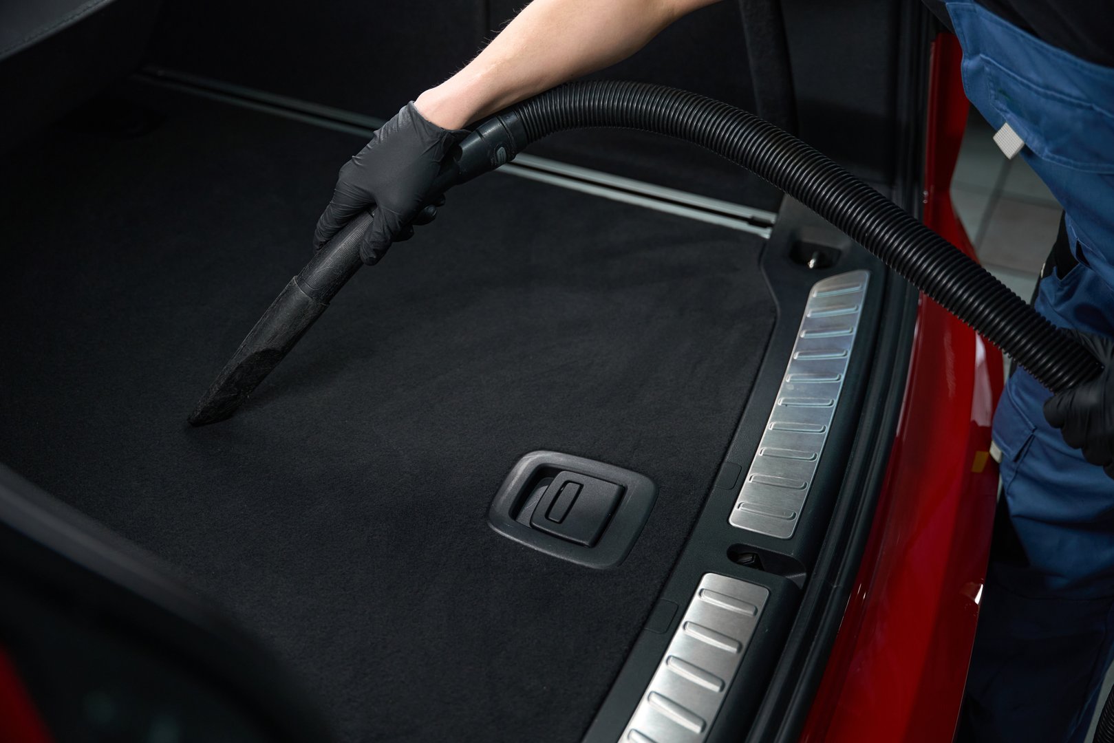 Cropped photo of detailer in nitrile gloves cleaning automobile trunk with vacuum cleaner