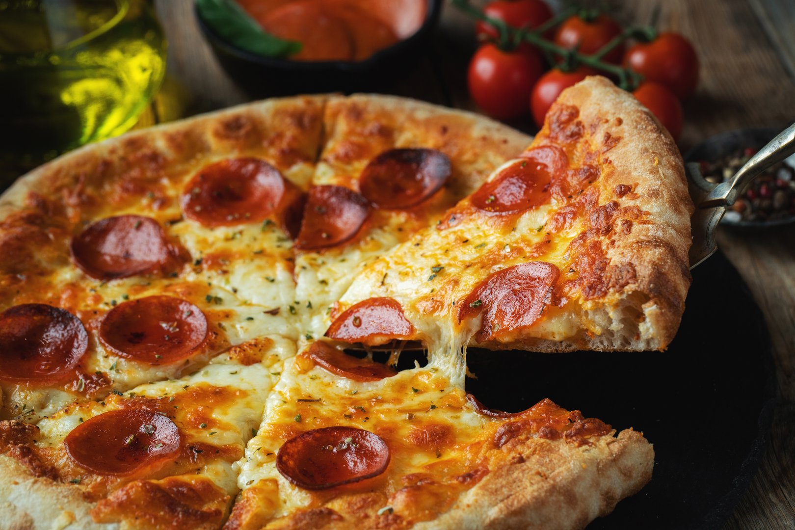 A slice of hot Italian pizza with stretching cheese. Pizza pepperoni on a dark wooden background.