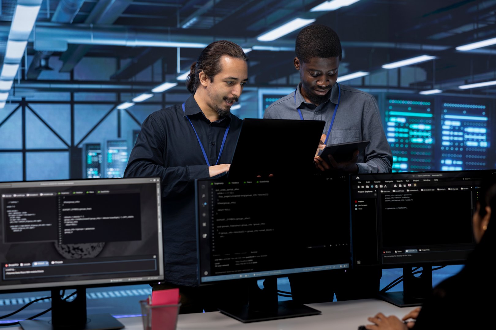 Coworkers in data center using laptop and tablet to find firewall misconfigurations affecting servers. Colleagues in server room checking systems bottlenecks leading to sluggish data transfer rates