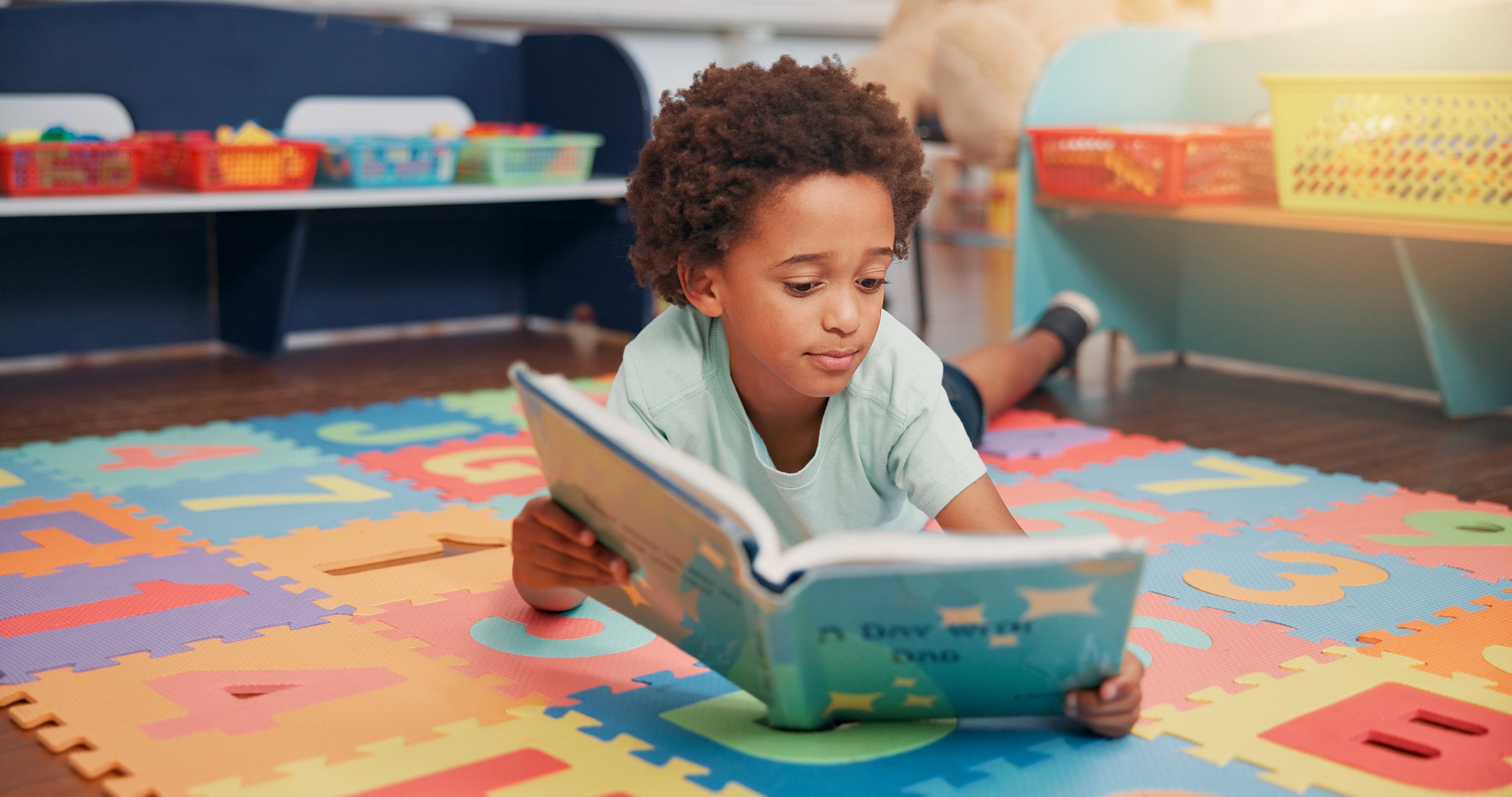 African boy, book and floor in classroom for development, storytelling and knowledge at academy. Child, learning and study on mat for scholarship, reading and info with course at elementary school