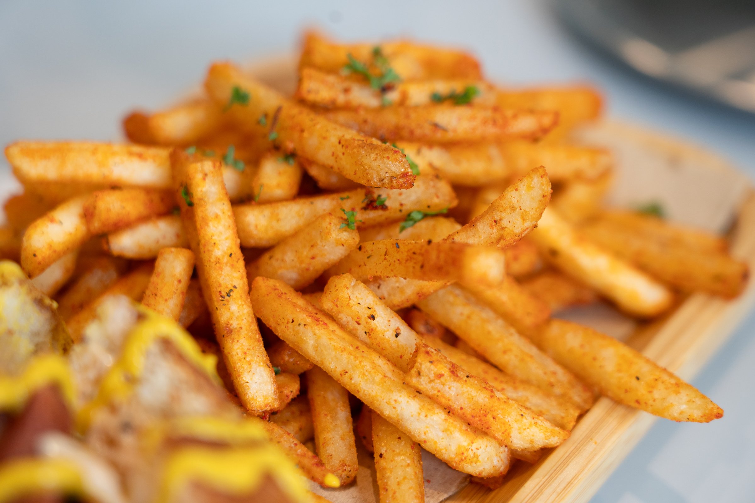 Golden crispy seasoned French fries served on a wooden tray, sprinkled with herbs and spices,