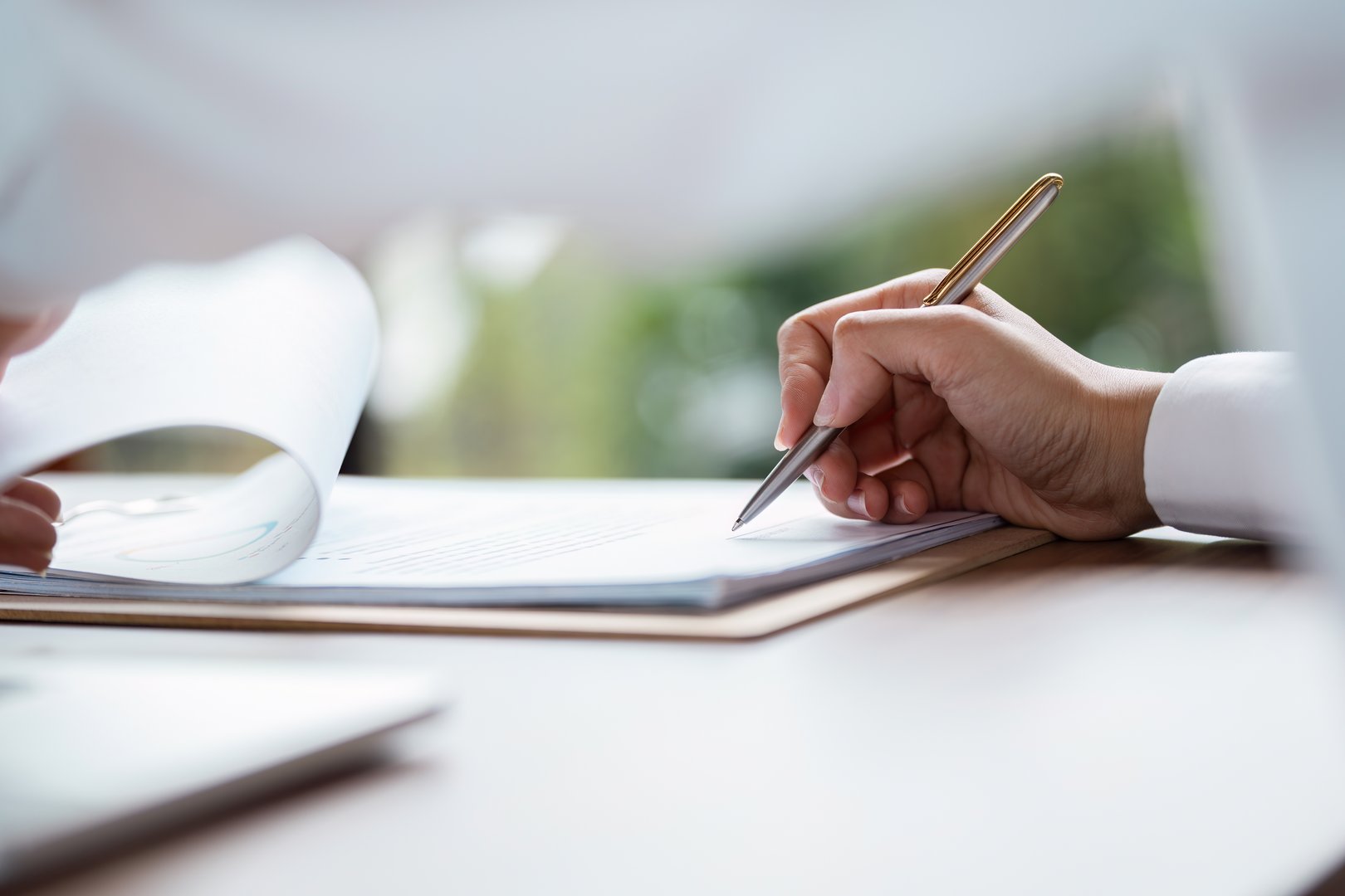 Close-up of a hand signing a business contract with a pen on a desk, symbolizing agreement and professional commitment.