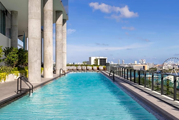 Rooftop swimming pool with glass railing, city skyline view, and seating area under a clear blue sky.
