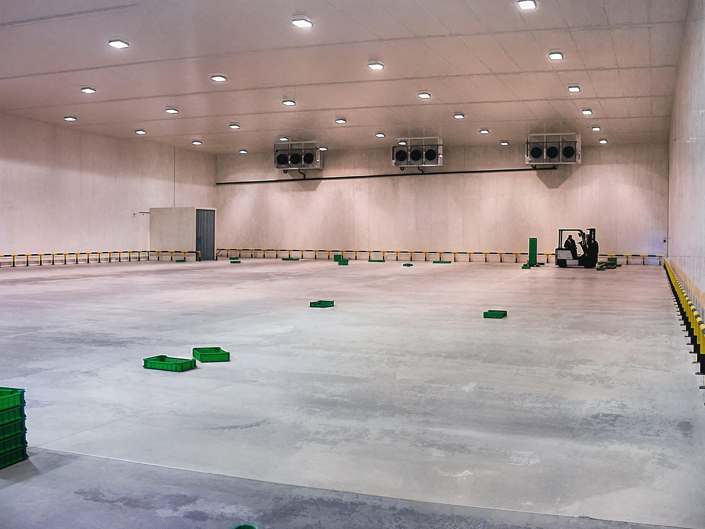 An interior shot of a vast cold storage warehouse with a forklift. The concrete floor reflects the overhead lighting.