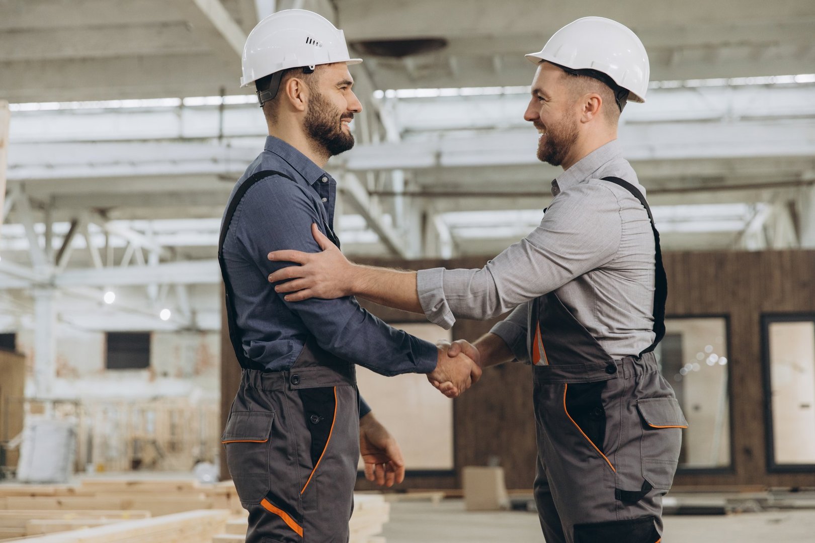 Two construction workers shaking hands after successfully assembling prefabricated house modules in modern factory