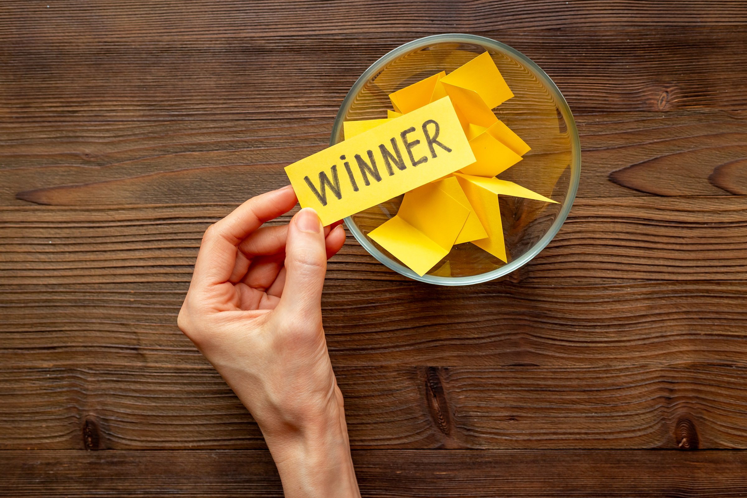 Hand is picking a winner ticket from glass jar, top view. Luck and lottery concept