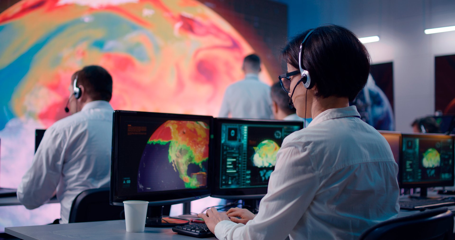 Young woman with headset typing on computer keyboard and speaking while researching global warming problem in office