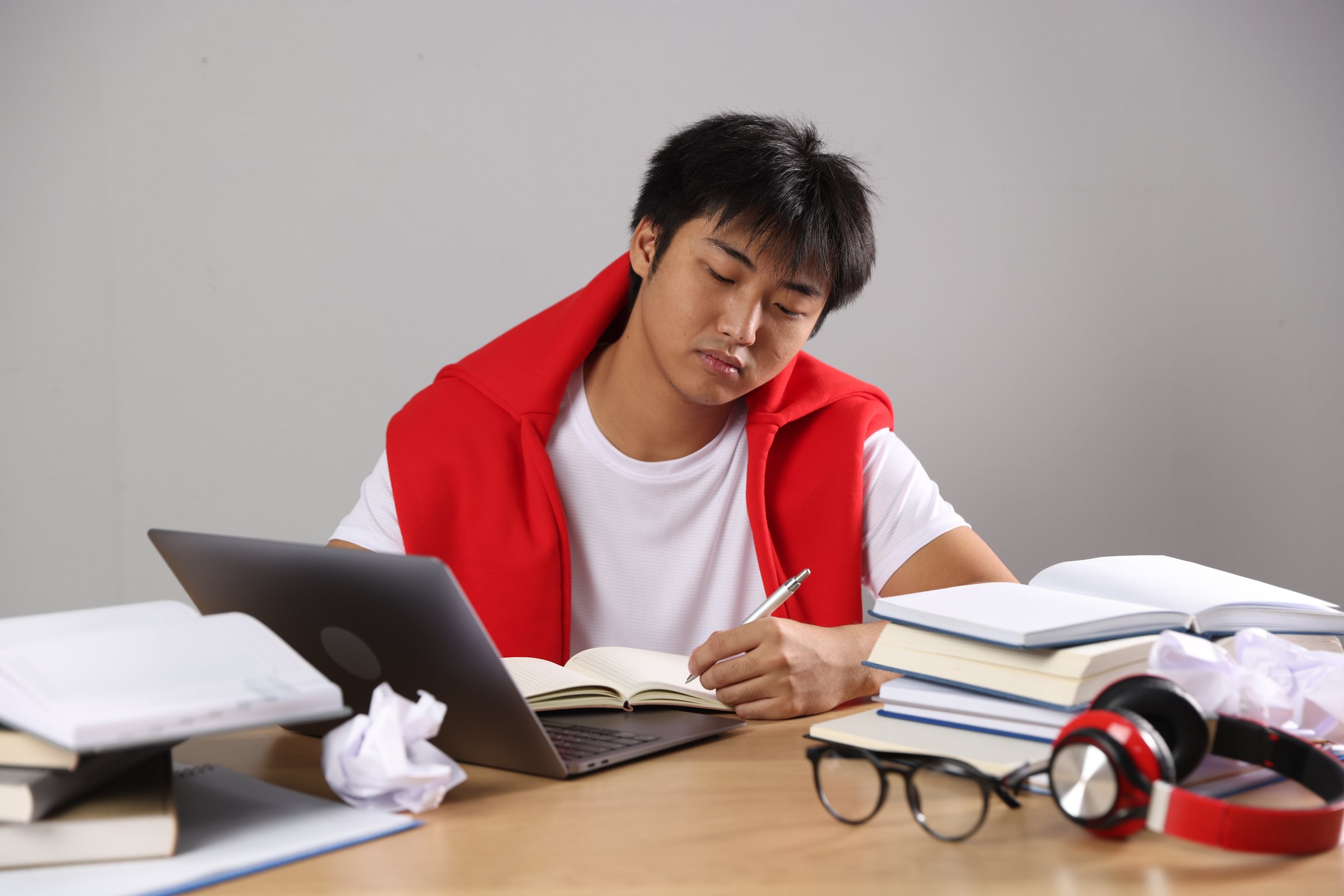 Student with laptop and books preparing for exam at wooden table near grey wall