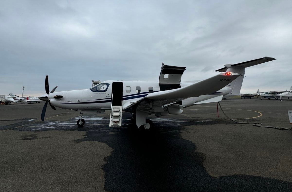 Small private jet with an open door on an overcast day, parked on a tarmac with other aircraft in the background.
