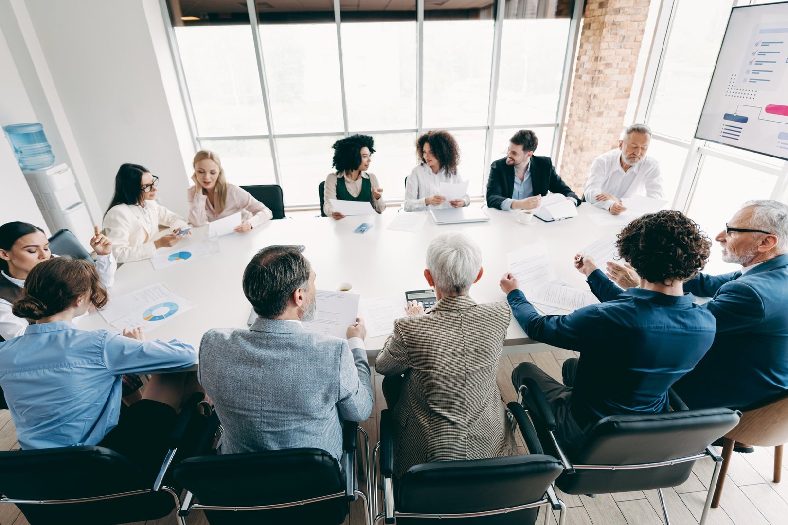 Diverse group of business professionals engaged in a collaborative meeting, exchanging ideas and insights, showcasing effective teamwork in a corporate environment.