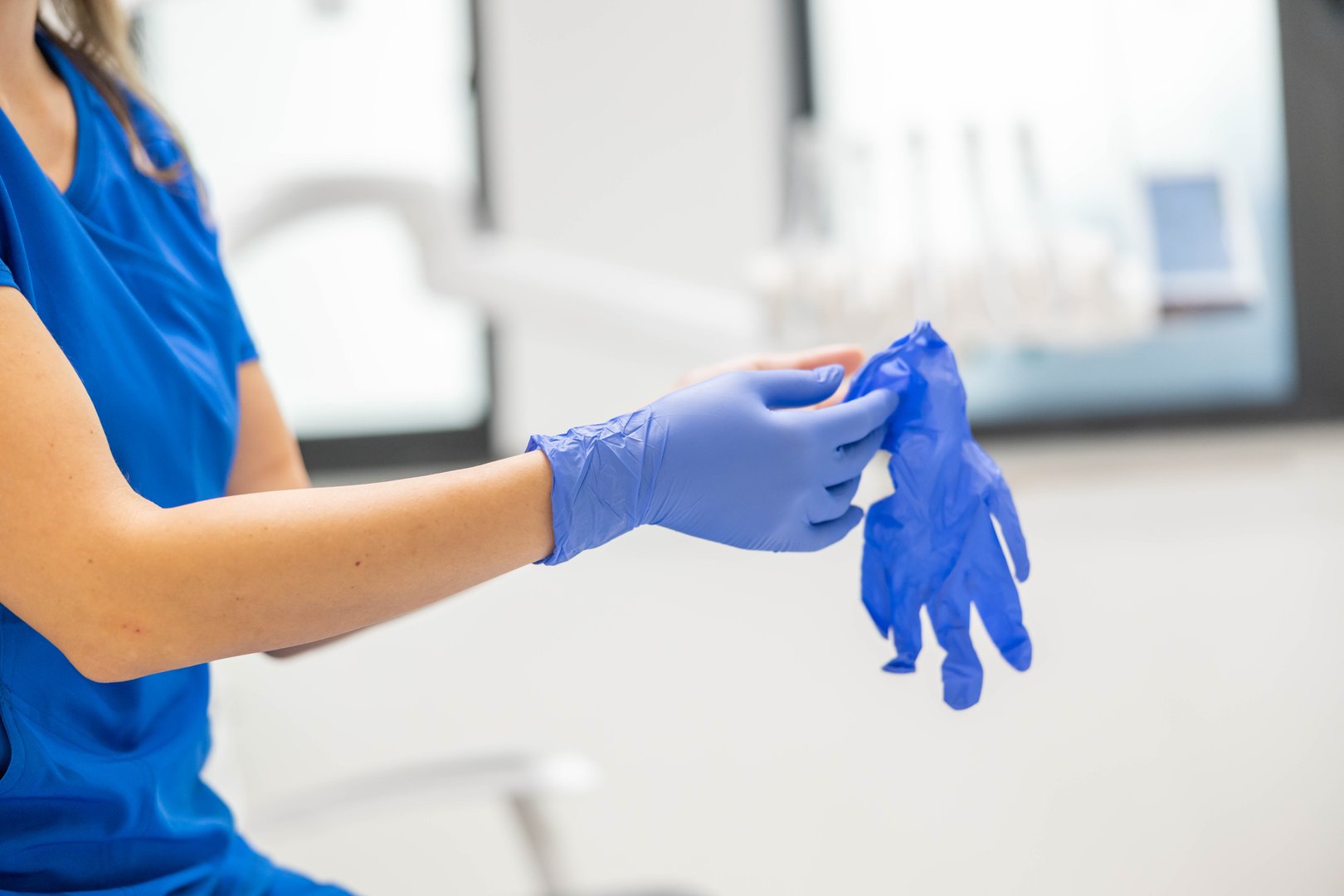 The image depicts a dentist preparing for a procedure by putting on blue disposable gloves, indicative of hygiene and professionalism in a modern dental clinic.