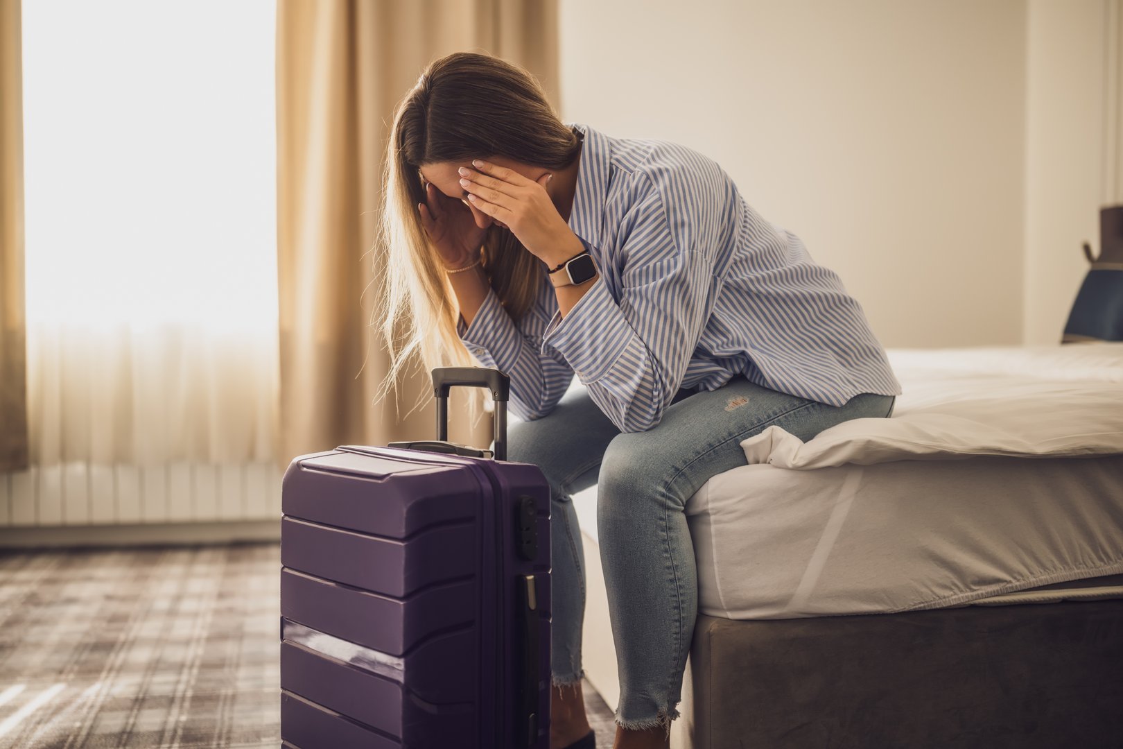 Tourist arrived in hotel room with her suitcase. She is tired of travel and needs rest.