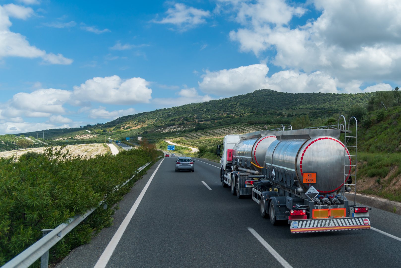 Tanker truck with trailer driving on the highway, with orange plates for dangerous liquids and corrosive panels according to ADR.