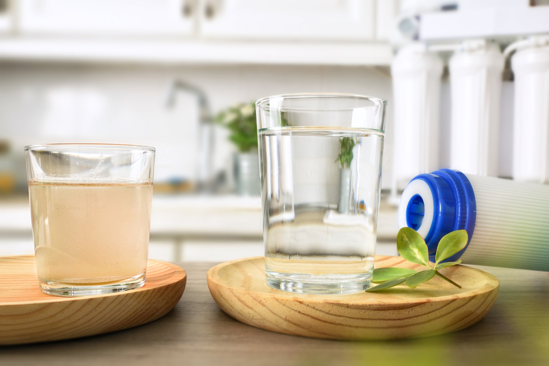 Comparison of dirty water and filtered by osmosis in glasses on a kitchen bench with filter and equipment in the background. Front view. Horizontal composition.