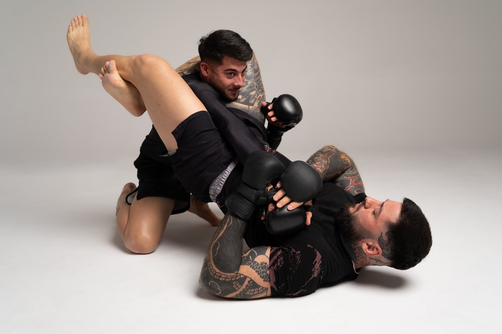 Two male mma fighters sparring intensely, with one applying a leg lock submission hold, showcasing skill and determination in combat