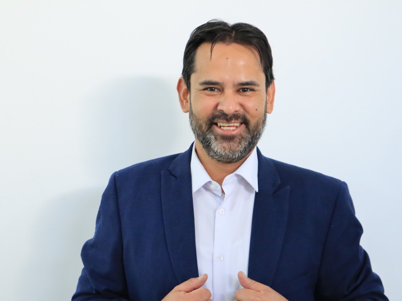 A man in a blue blazer and white shirt smiling against a plain white background.