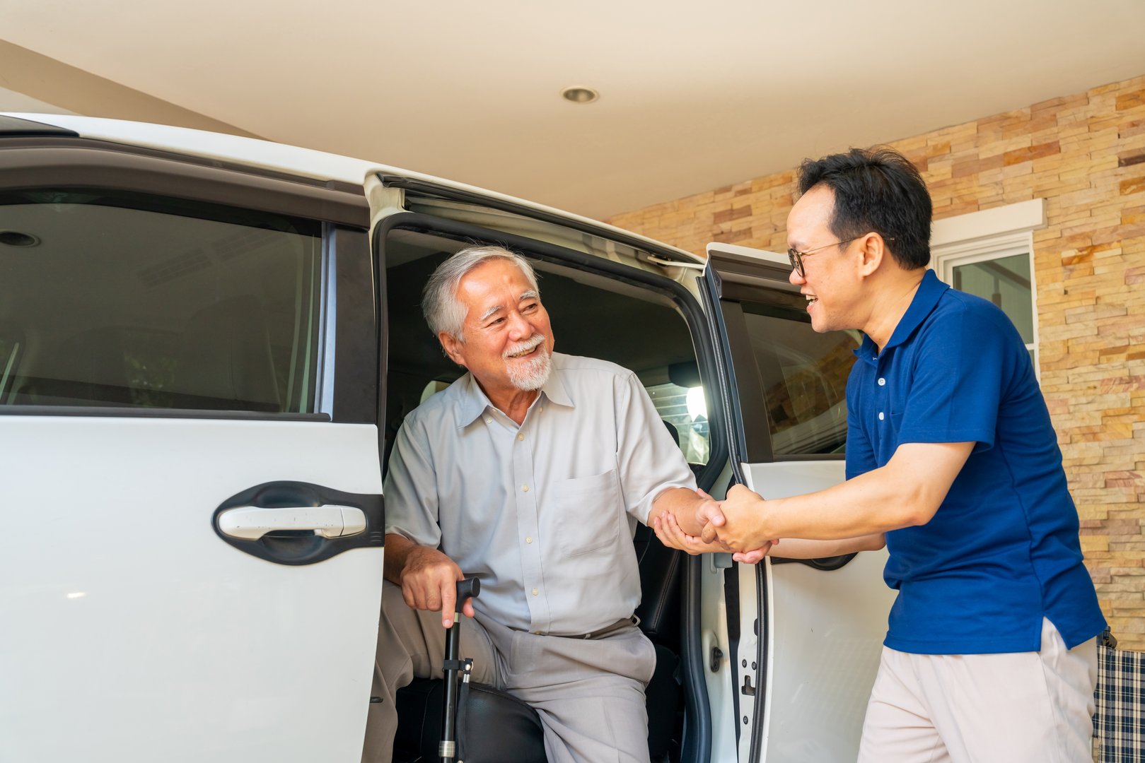Asian man caregiver or taxi driver helping senior man patient get in the car to get to medical appointments or healthcare therapy sessions at hospital. Assisted elderly patient transportation services