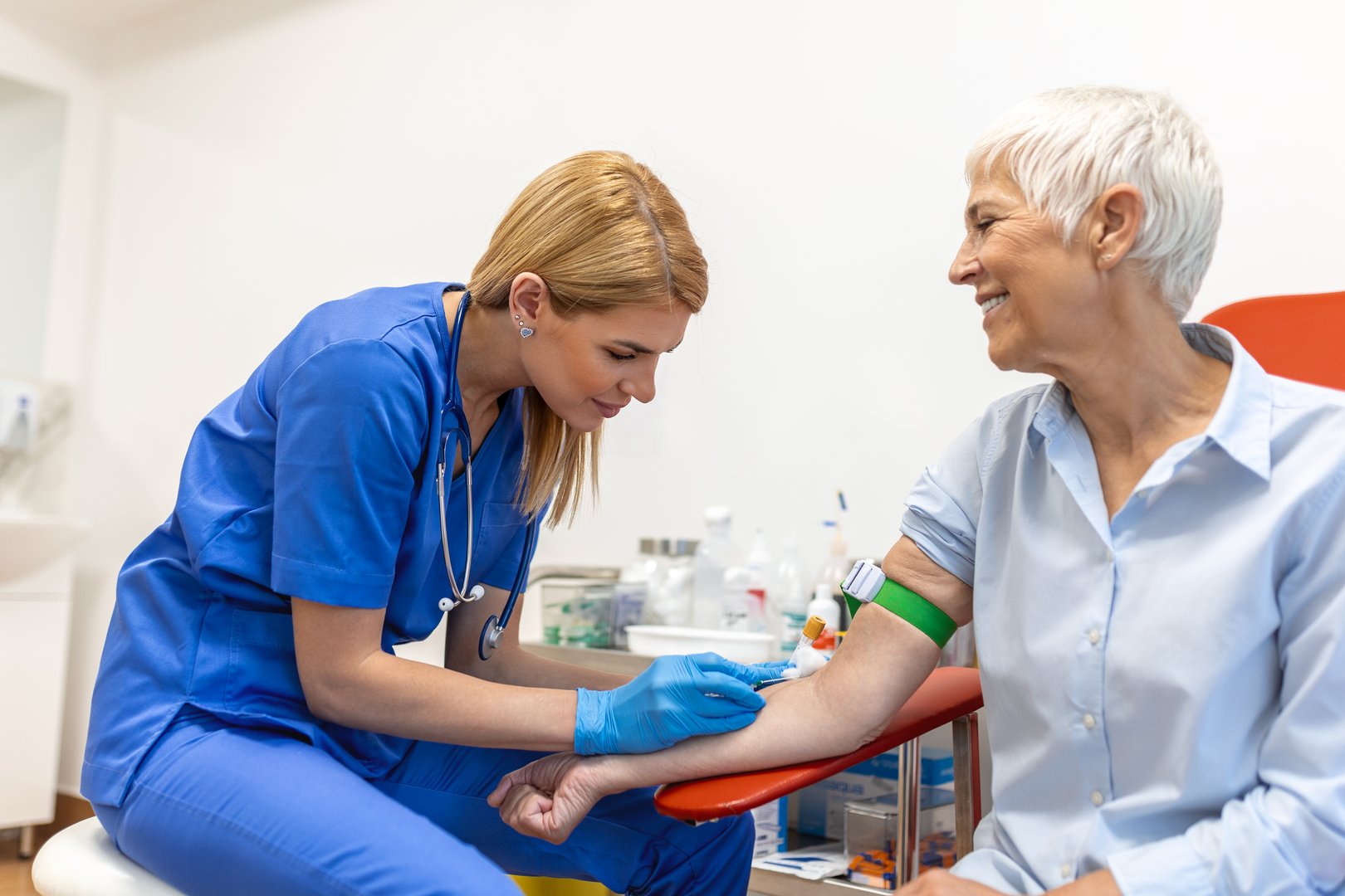 Preparation for blood test with senior woman by female doctor medical uniform on the table in white bright room. Nurse pierces the patient&#039;s arm vein with needle blank tube.