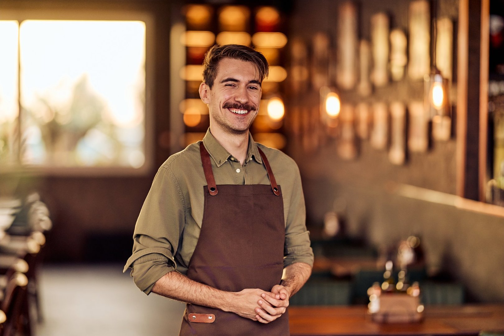 Smiling server posing in a cozy restaurant environment with warm, ambient lighting.