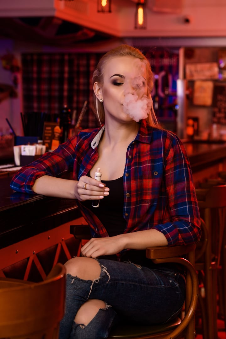 Young pretty woman smoke an electronic cigarette at the vape bar. Vape shop.