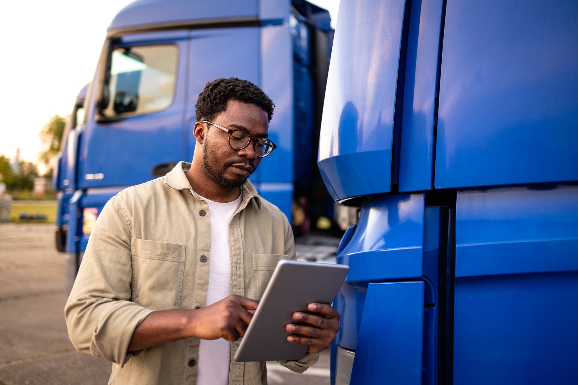 Professional driver standing by his truck and checking route on his tablet computer.