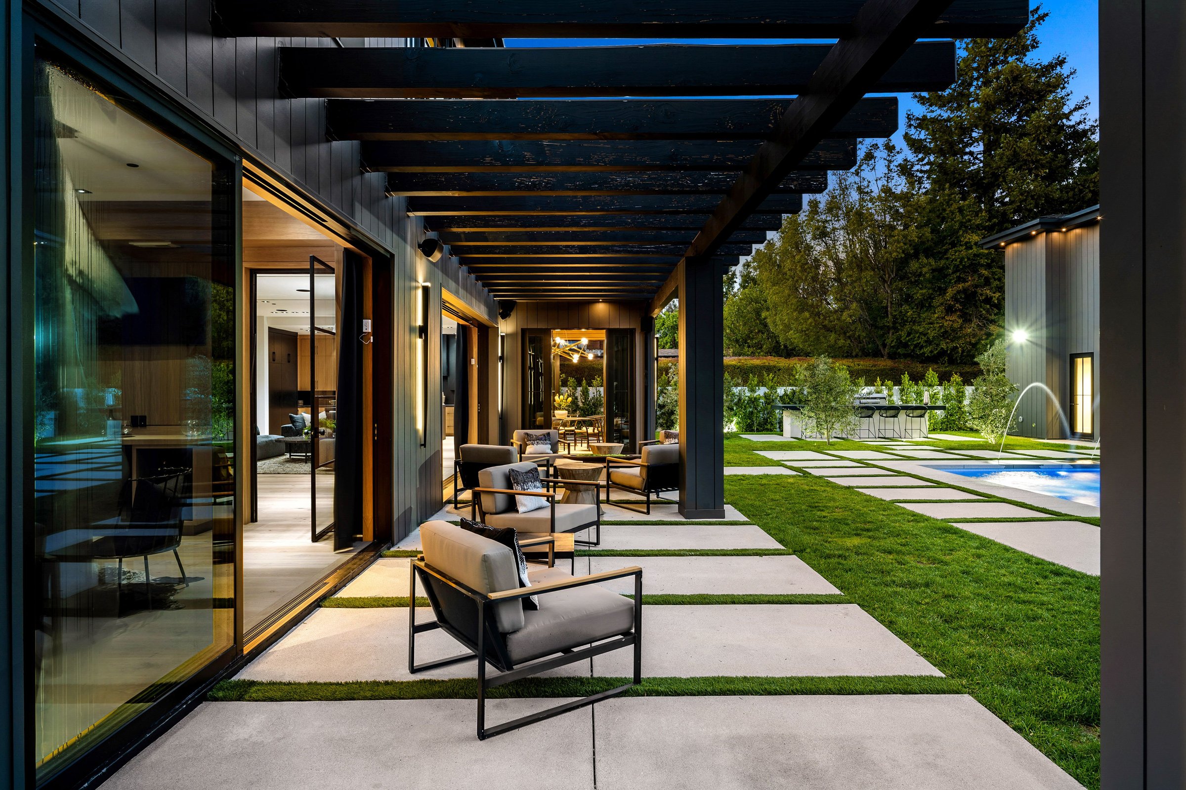 Modern outdoor patio area with comfortable seating, pergola, and well-manicured lawn in the evening light.