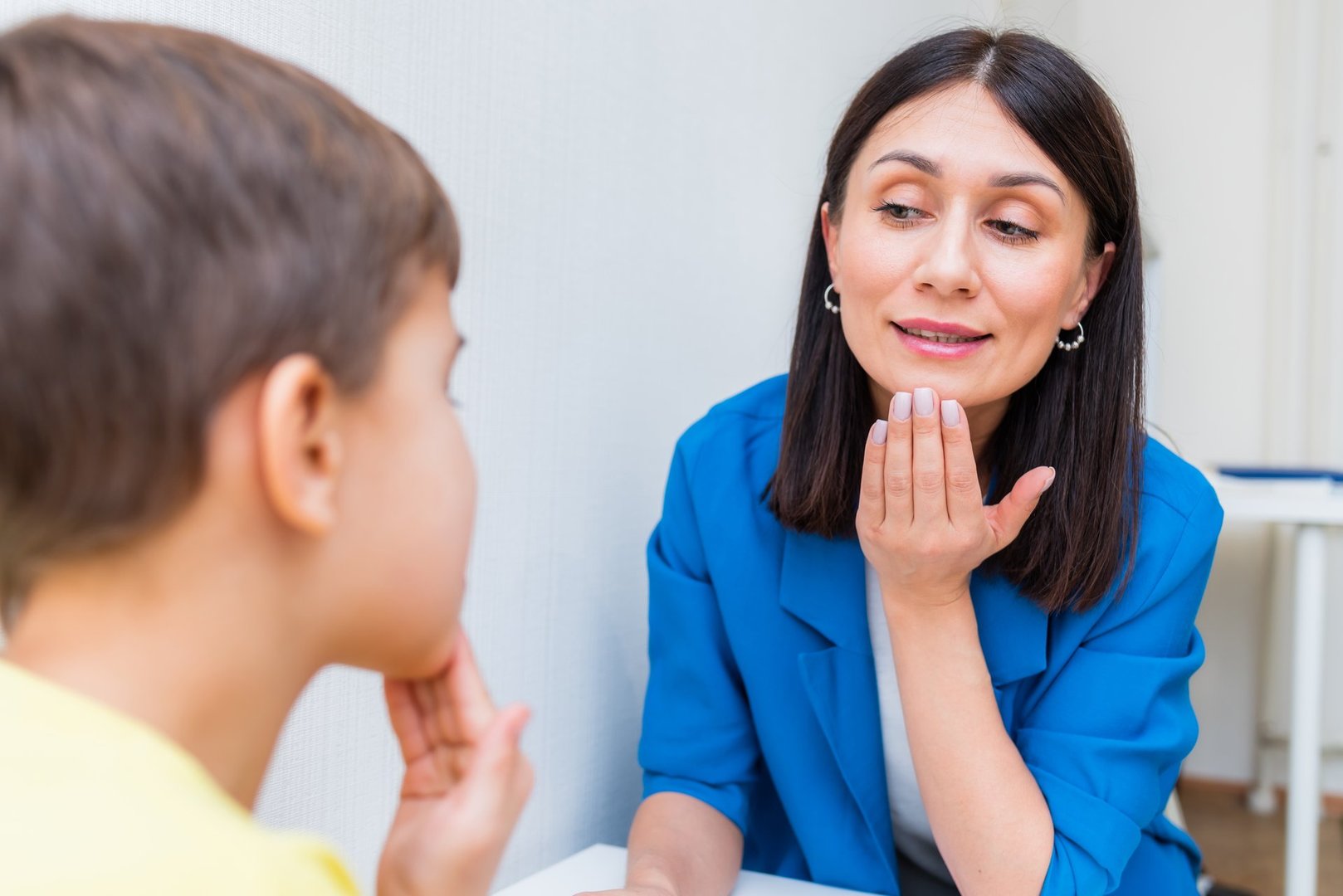 Woman speech therapist helps a child correct the violation of his speech in her office