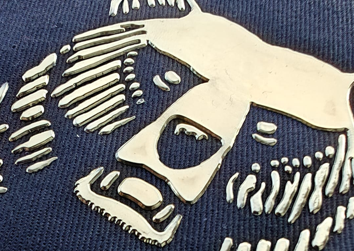Metallic bear face design on navy blue fabric, featuring textured and smooth surfaces for contrast.