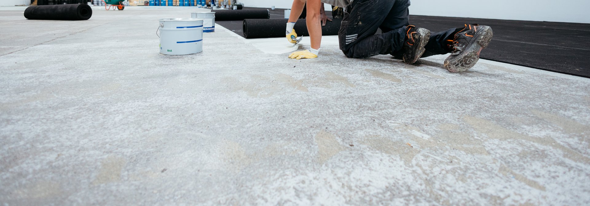 Construction worker on his knees applying waterproof tape to a rooftop cement foundation
