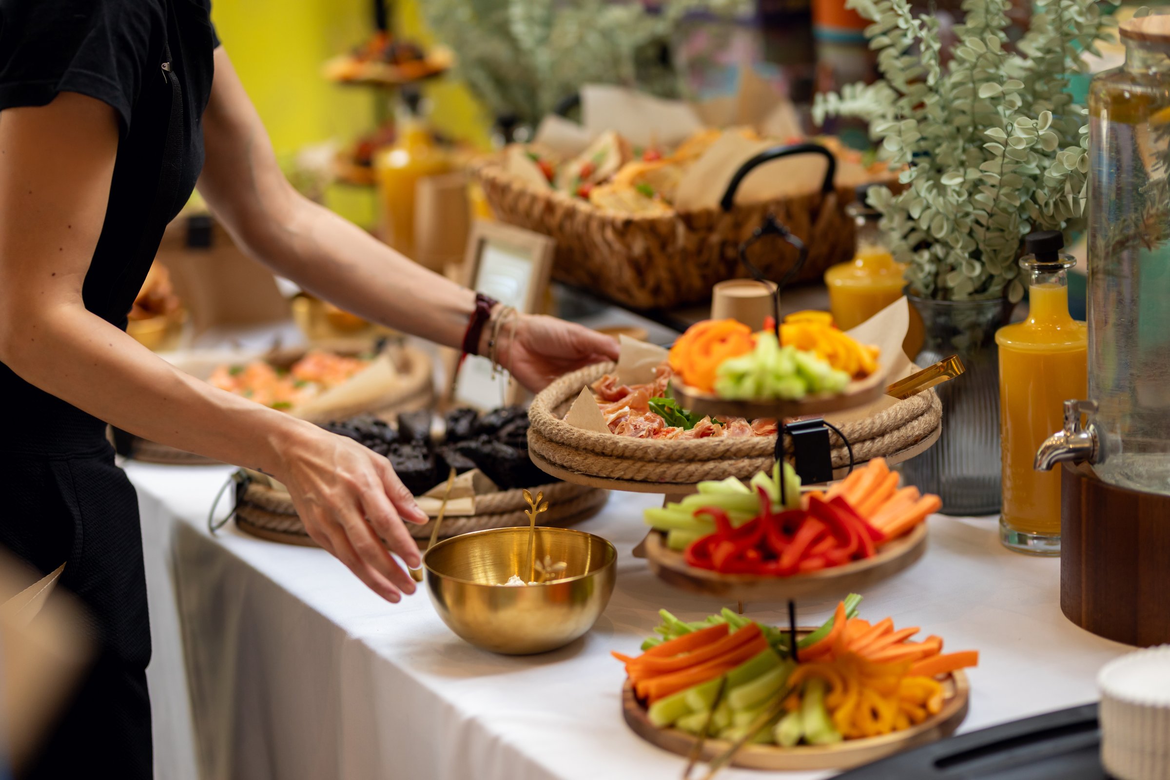 Professional caterer arranging buffet with colorful sandwiches, fresh vegetables, and tempting desserts at catering event