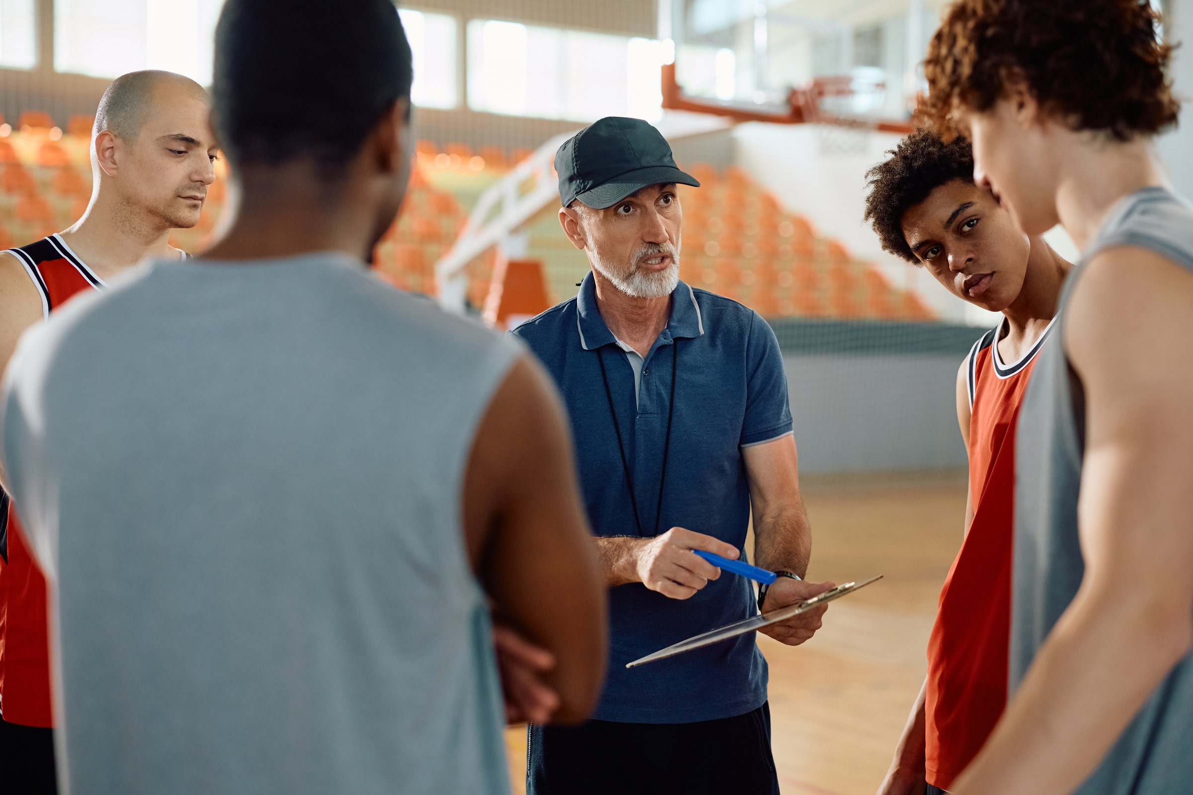 Mature coach explaining game tactics to basketball players during sports training.