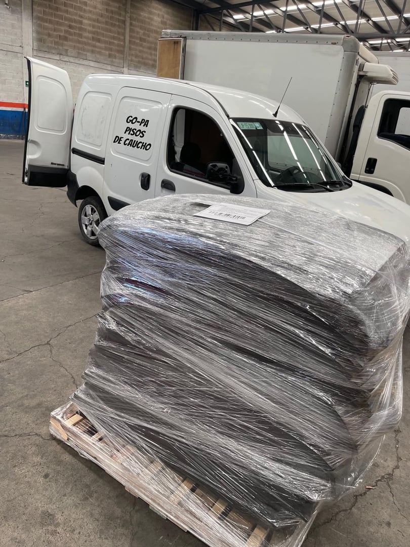 Pallet of rubber mats wrapped in plastic next to a white van in a warehouse with an open door.