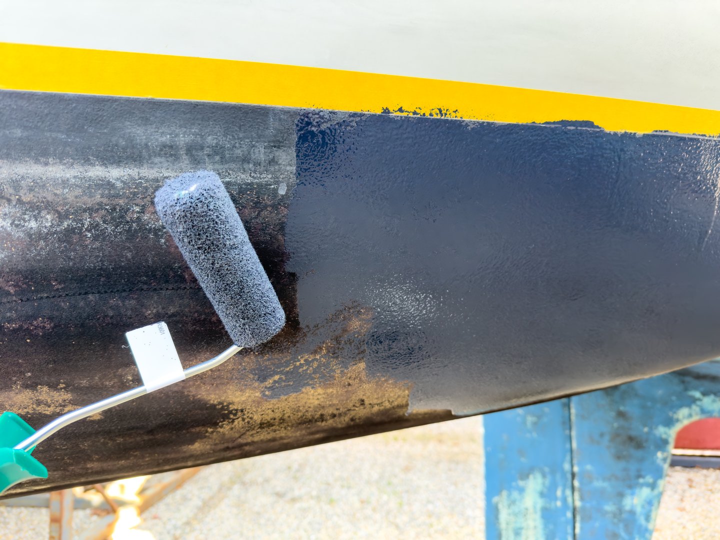 Sailing boat on stilts being painted with antifouling in boatyard