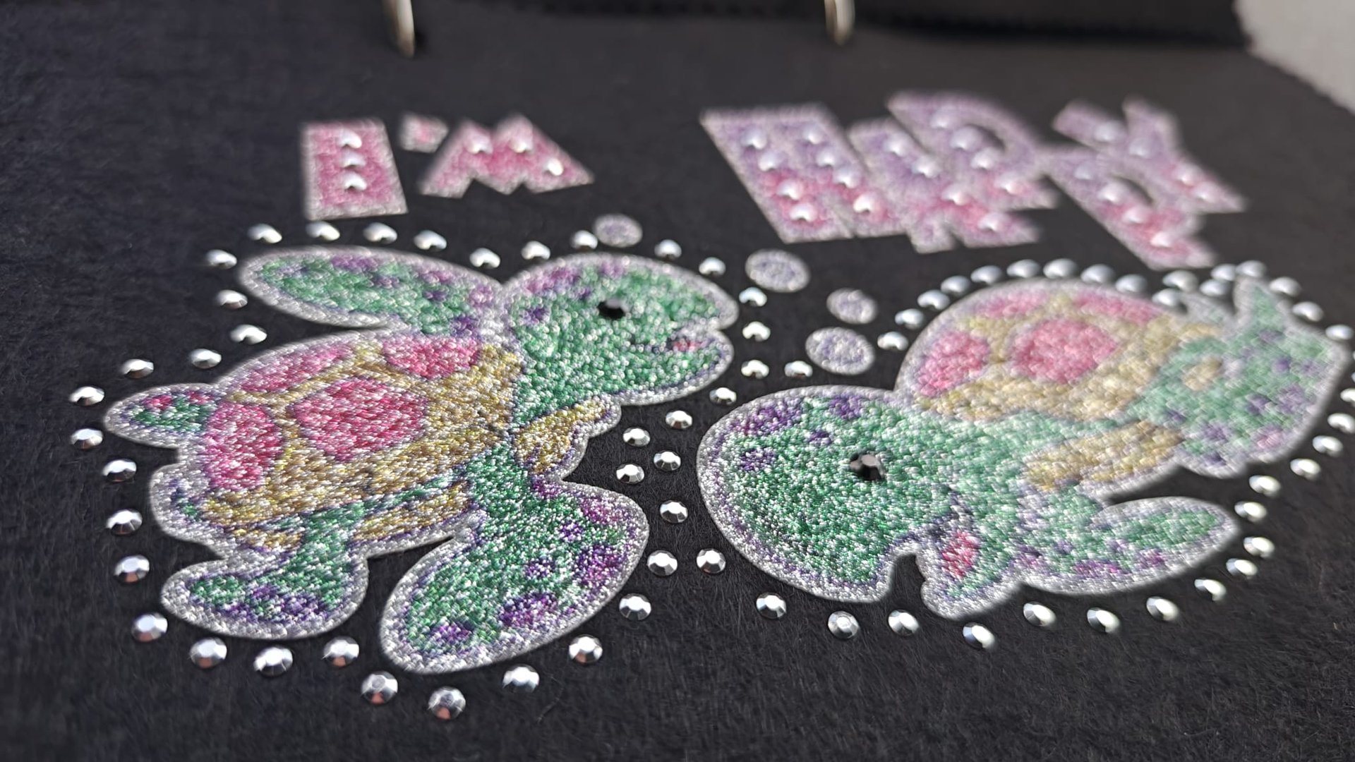 Glittery images of two turtles with colorful shells on a black background surrounded by small rhinestones.