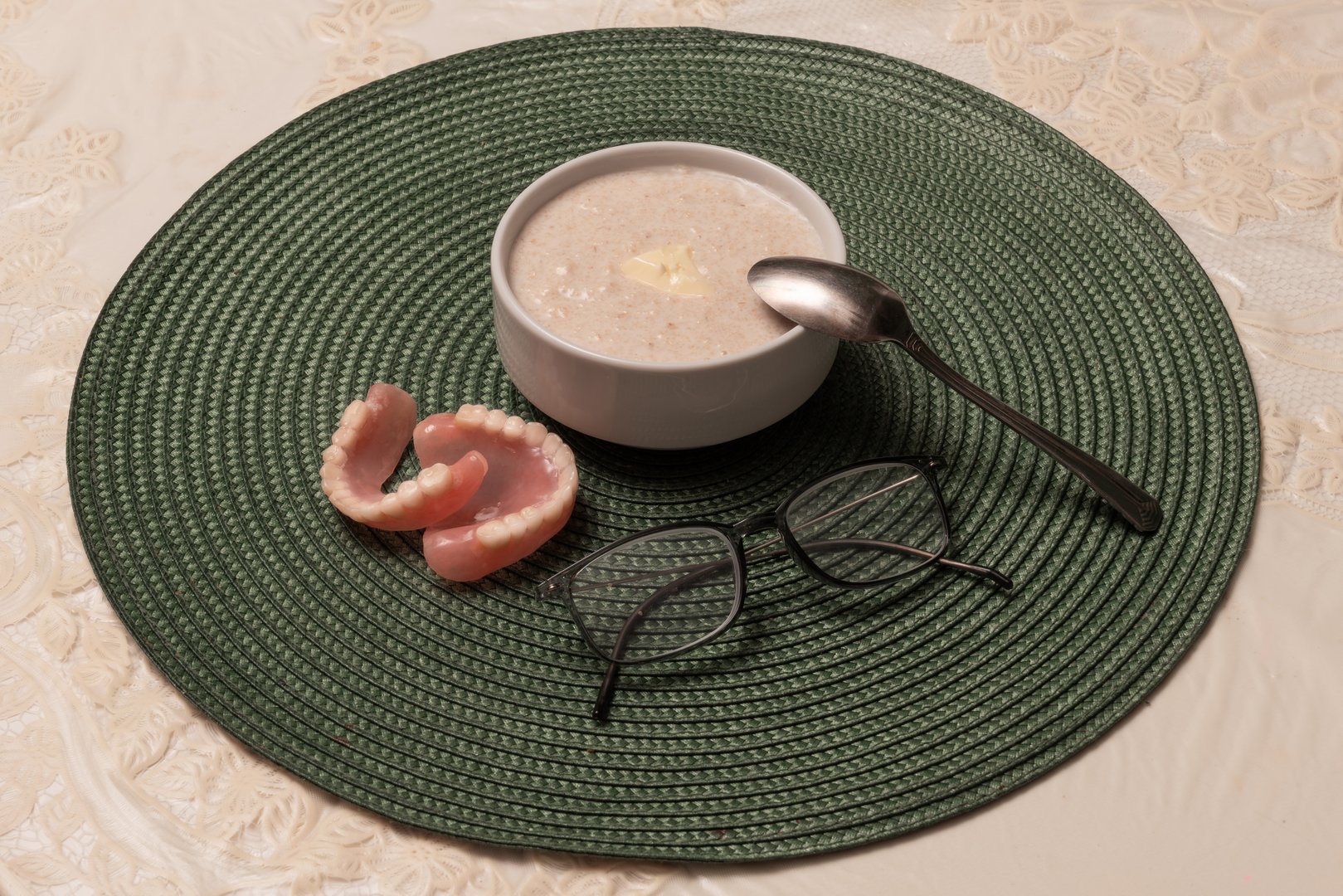 Artificial dentures for a person, reading glasses and a plate of porridge on a table